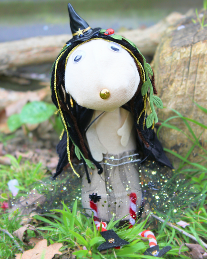 Finished Punky witch sock puppet sitting in grass beside a tree, wearing a black hat and glittery tutu